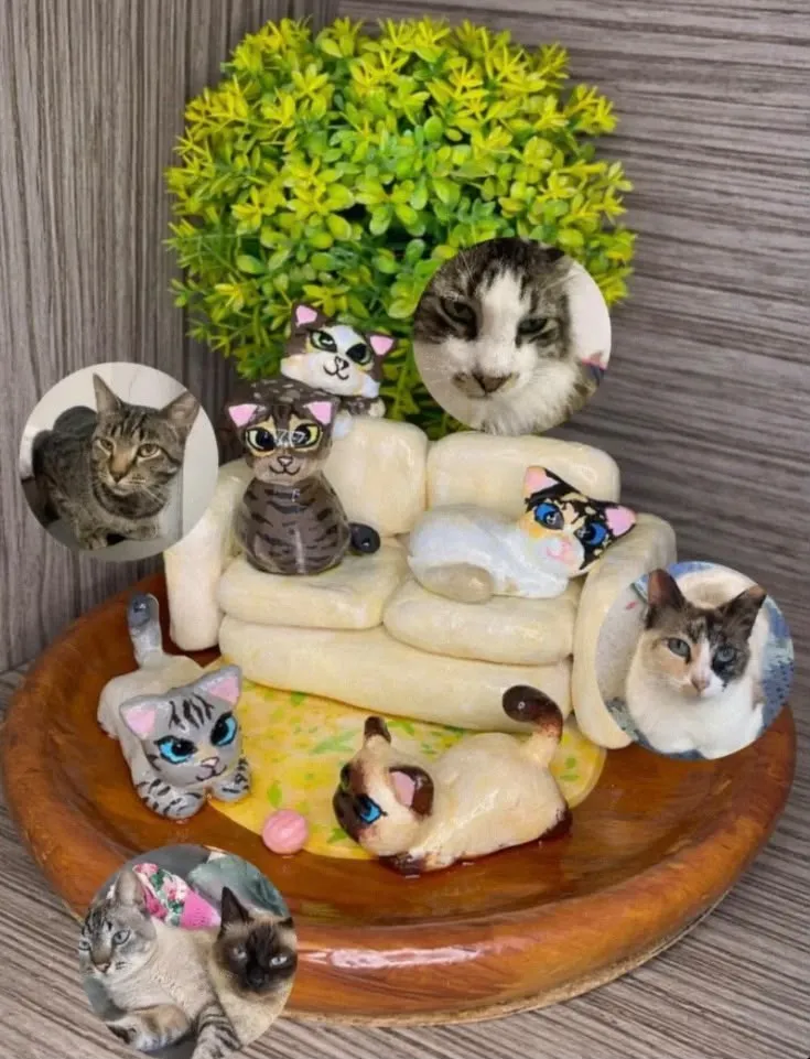 Miniature clay sculpture of five cats on and around a cream sofa on a wooden base, shown next to photos of the real cats it was modelled on.