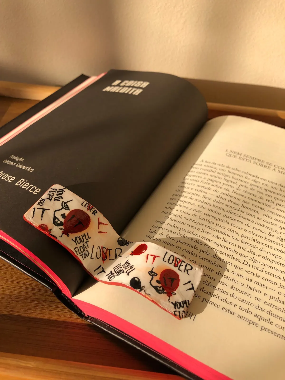 Hand-painted white bookmark with red balloons and the words "You'll float too" and "LOSER" lying across the pages of an open book.