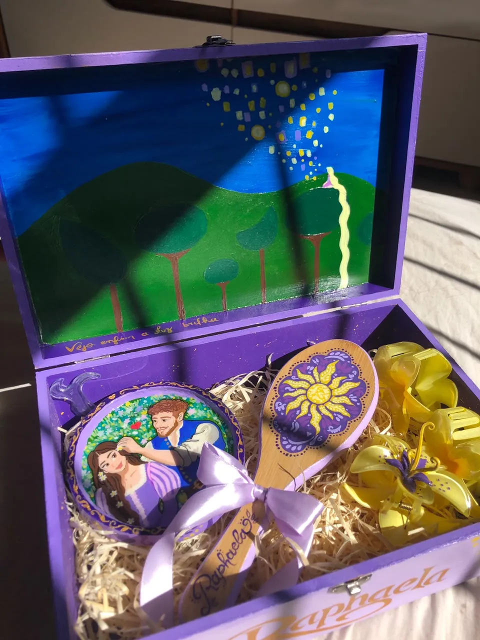 Open purple wooden keepsake box painted with the Tangled lantern scene inside the lid, holding a painted hairbrush, a hand mirror with Rapunzel and Flynn, and yellow hair clips.