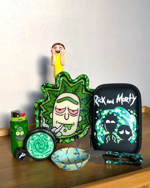 Hand-painted Rick and Morty themed set on a wooden table, a green Rick tray, portal grinder, Pickle Rick lighter, black painted case and a small Morty figure.